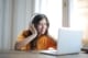woman in orange shirt sitting by the table using macbook 3808021